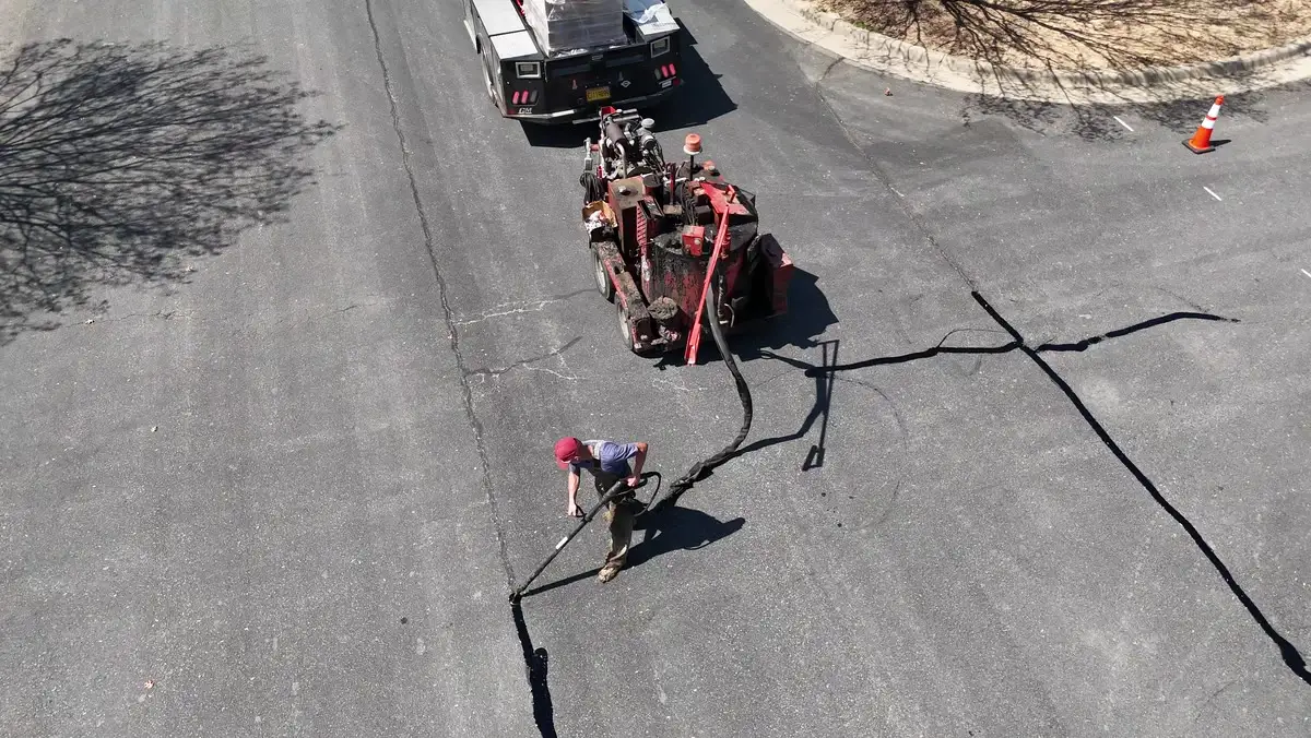Aerial view of an Arkansas Pavement crew crack-sealing a road, the sealing rig and hose run out behind the worker