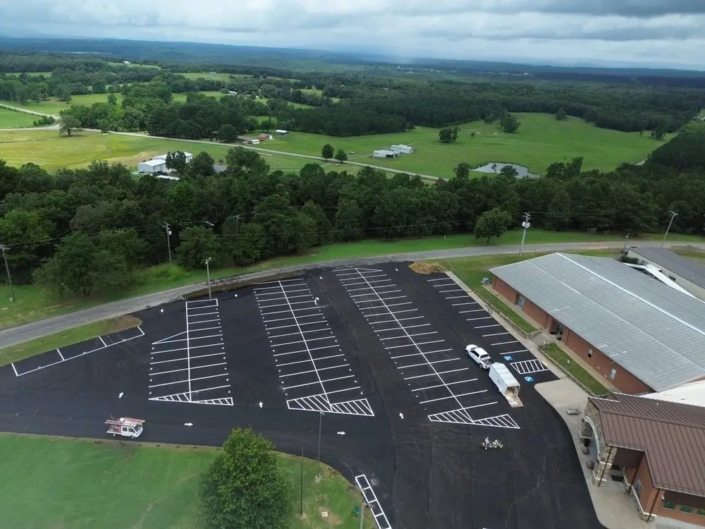 Aerial view of a school lot with long runs of new white stalls above a green valley