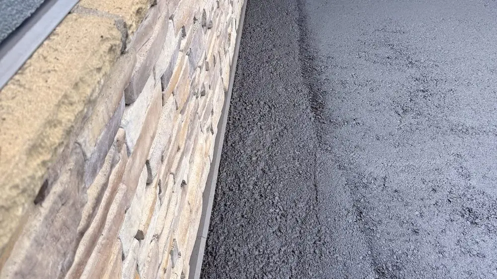 Fresh asphalt laid up to a stone building wall