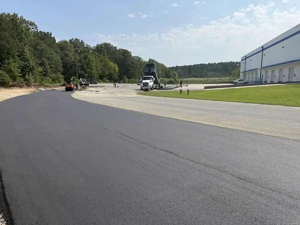A paver and roller laying a new asphalt road surface alongside a commercial building