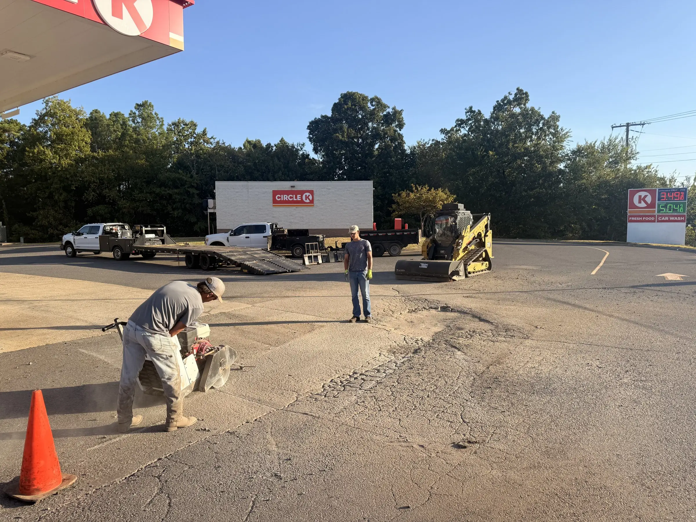 An Arkansas Pavement crew member cutting out a failed section of asphalt at a forecourt, cones set around the work