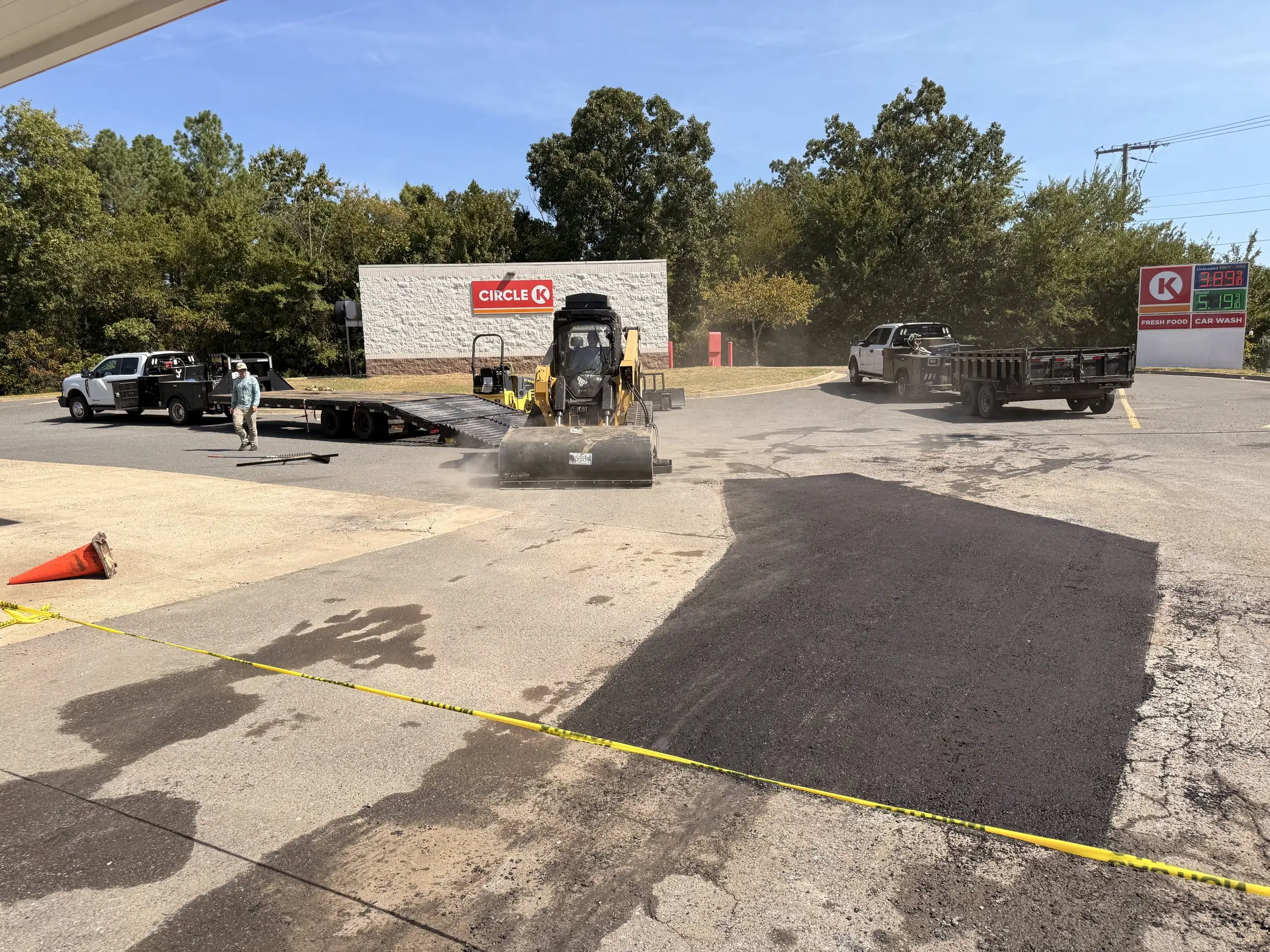 A freshly laid asphalt patch being rolled at a forecourt, the new mat dark against the older surface around it