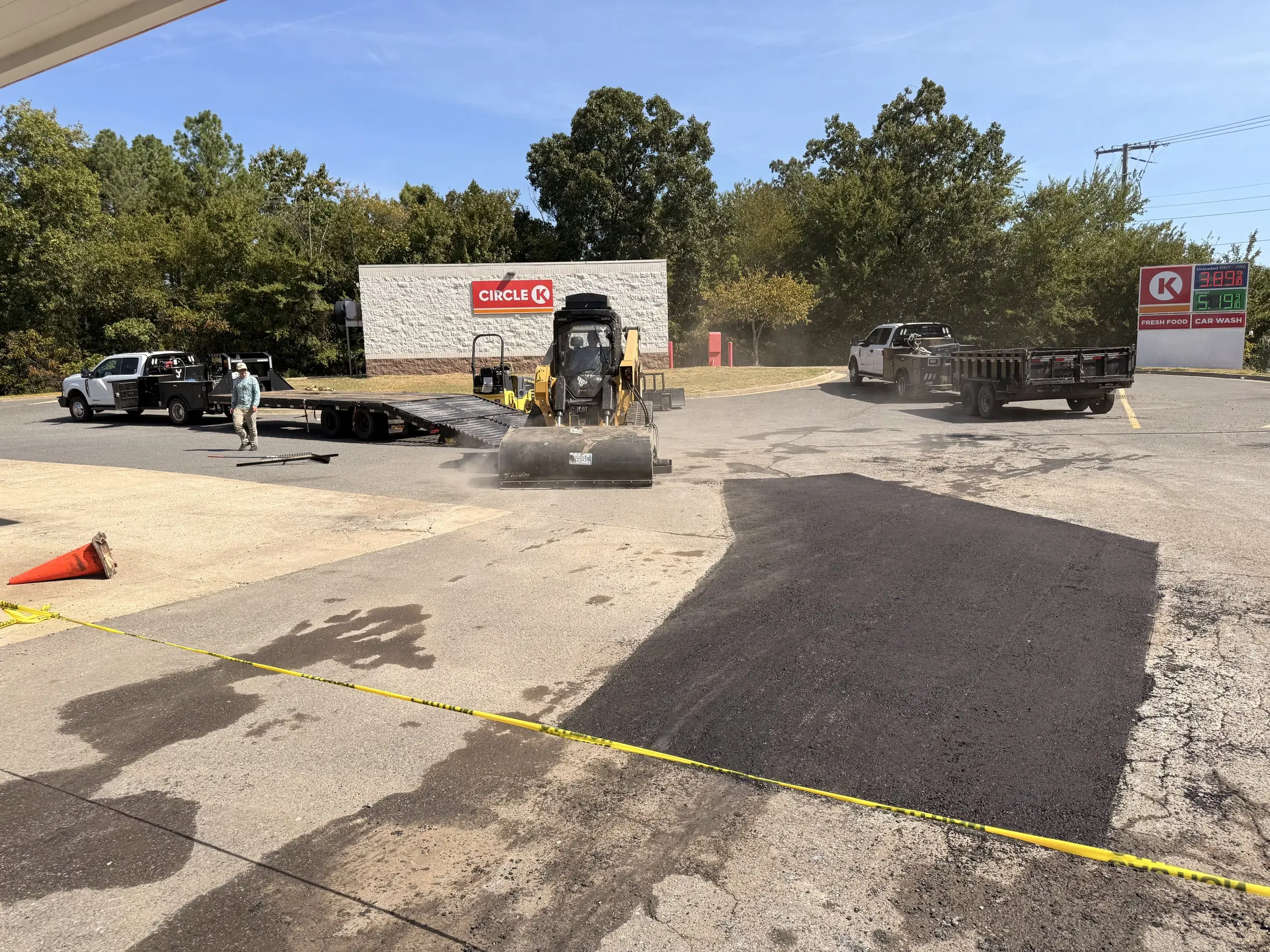 A freshly laid asphalt patch being rolled at a forecourt, the new mat dark against the older surface around it