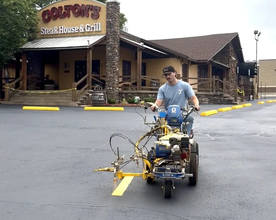 An Arkansas Pavement crew member riding the line striper, laying a fresh yellow line across a restaurant parking lot